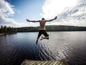 Young man jumping off a dock into a lake