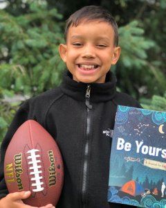 Boy holding a football in one hand and a Be Yourself Journal in another