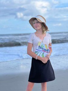 Girl standing on the beach holding a Be Yourself Journal for Catholic girls